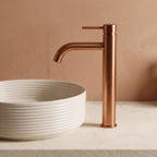 Robinet lavabo Dora Or Rose Brossé modèle haut vu de profil à côté d'une vasque à poser