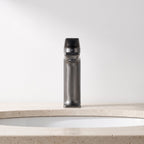 Robinet lavabo Metra Gun Metal modèle court vu de face sur un plan en travertin