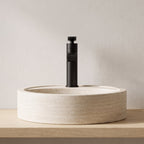 Robinet lavabo cascade Vetra noir mat sur une vasque en travertin